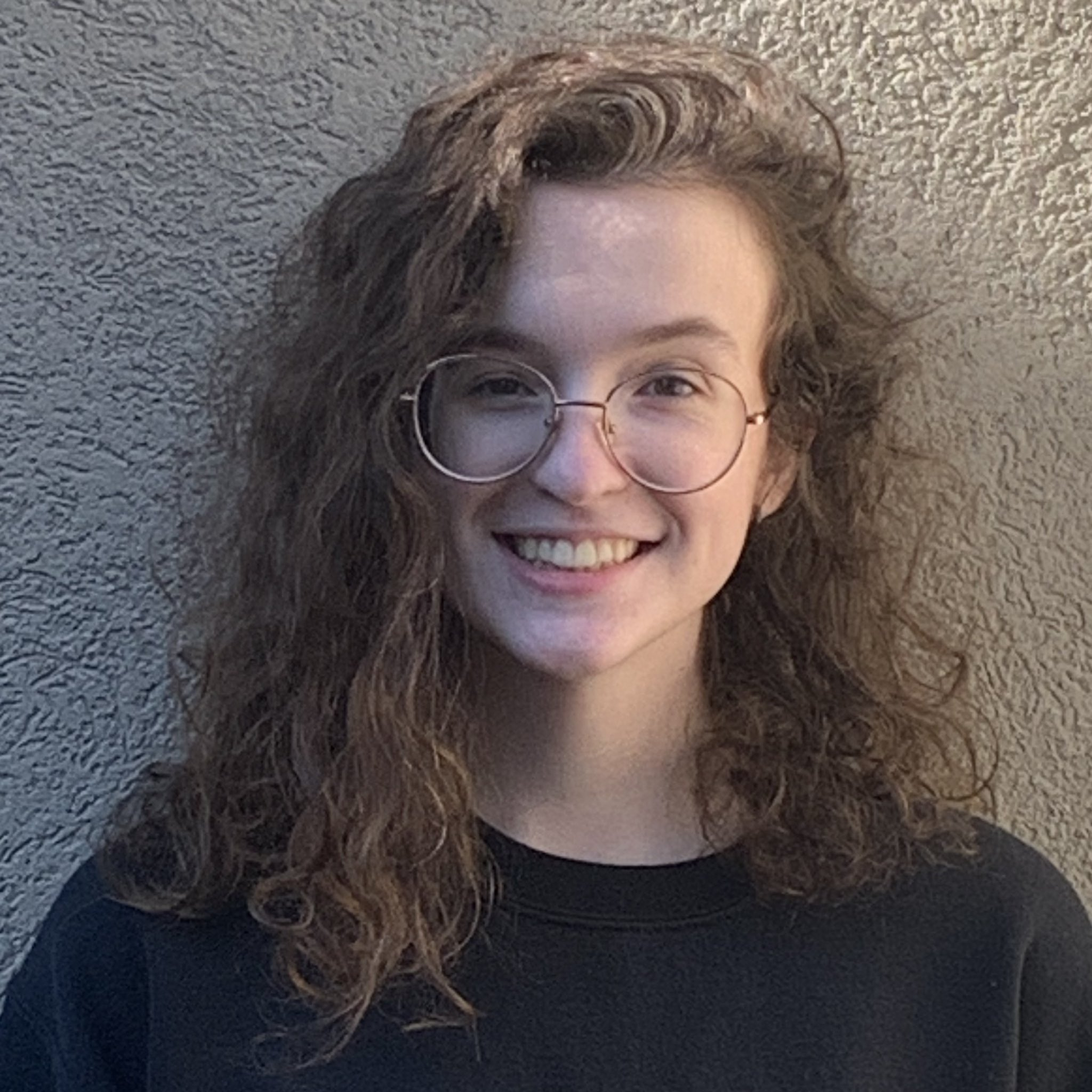A young woman wearing glasses and a black shirt is smiling.