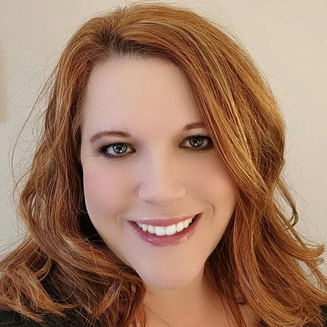 A woman with red hair and green eyes is smiling for the camera.