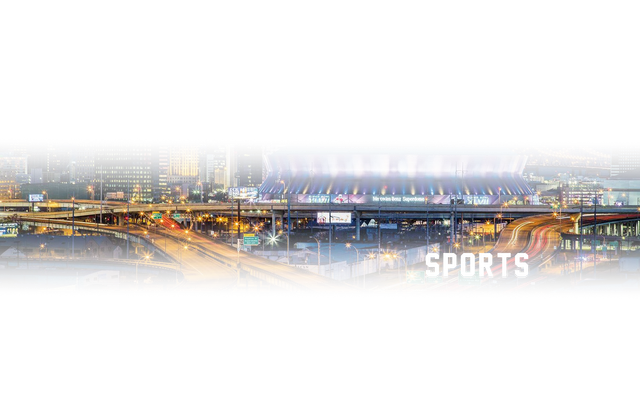 An aerial view of a city at night with a stadium in the background.