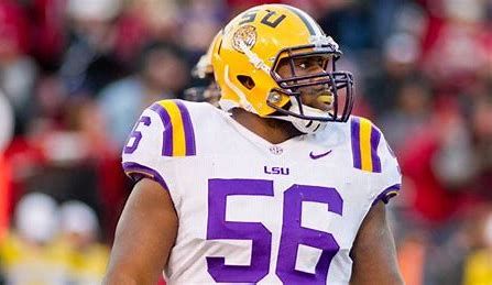 A football player wearing a helmet and a purple and white uniform is standing on the field.