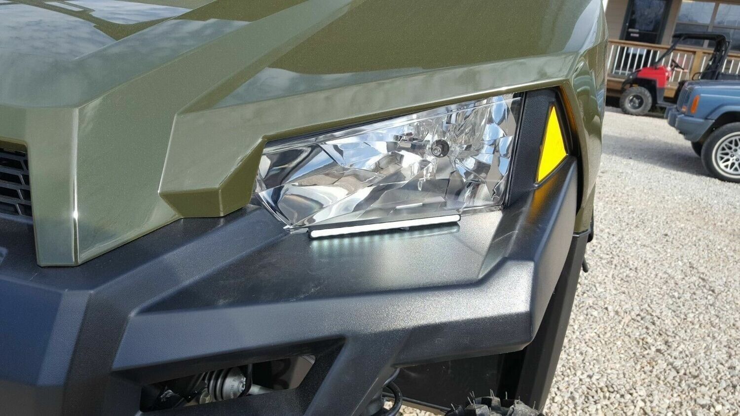 A close up of a green vehicle 's headlight on a gravel road.
