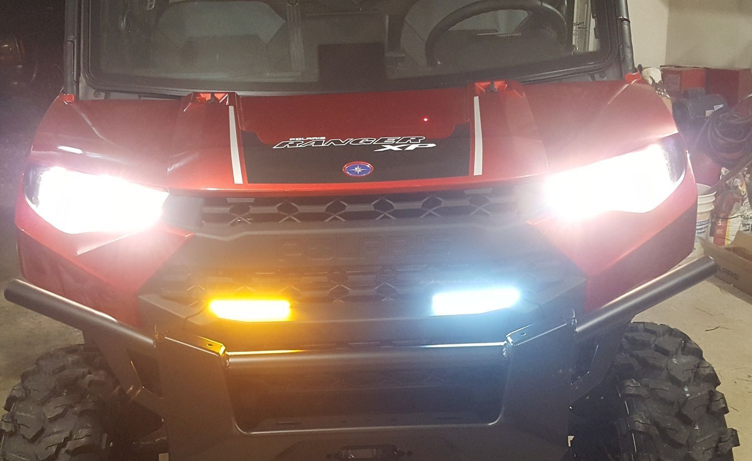 A red atv is parked in a garage with its lights on.