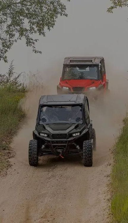 Two atvs are driving down a dirt road.