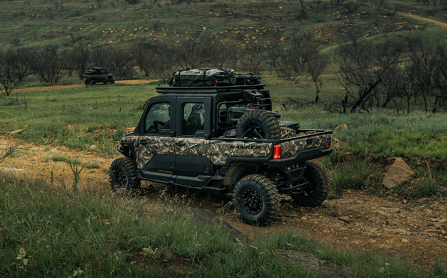 A can am defender is driving down a dirt road in a field.