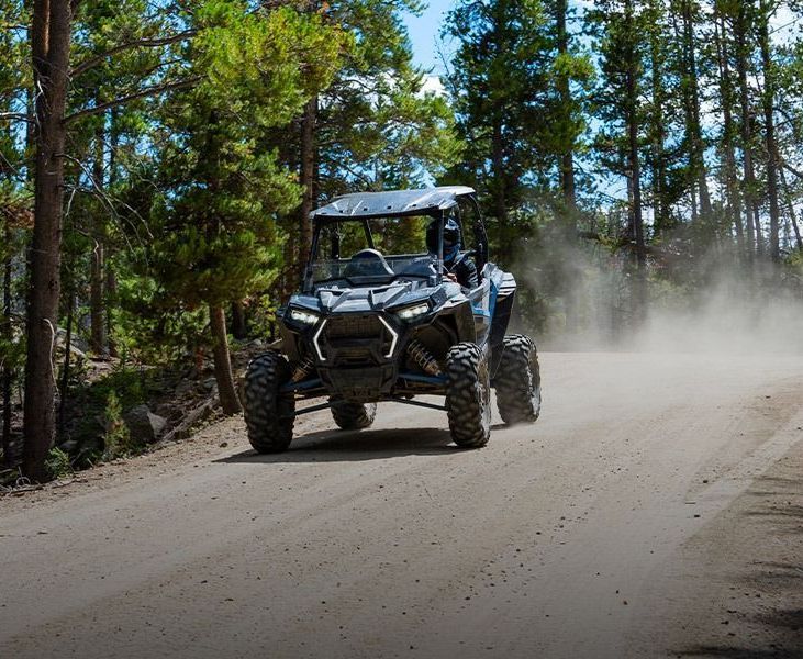 A polaris atv is driving down a dirt road in the woods.