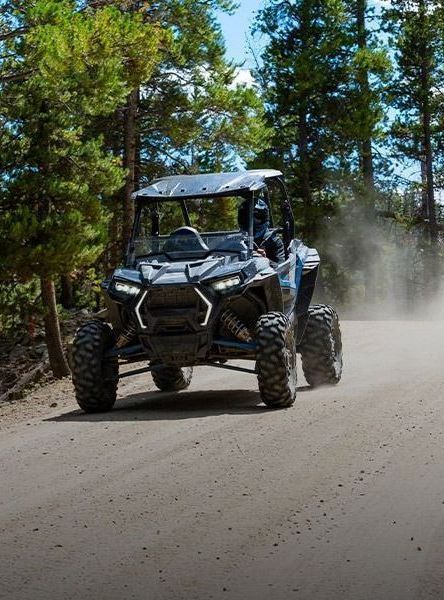 A polaris atv is driving down a dirt road in the woods.