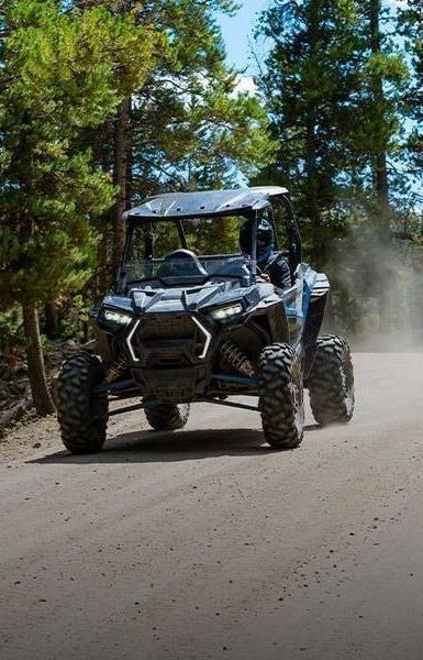 A polaris atv is driving down a dirt road in the woods.
