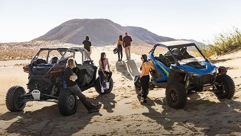 A group of people are standing next to two atvs in the desert.