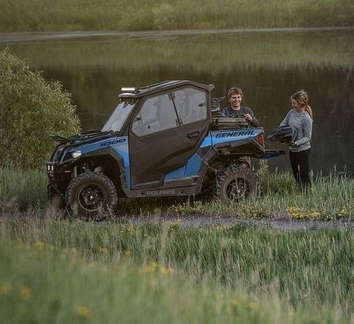A man and a woman are standing next to a blue atv.