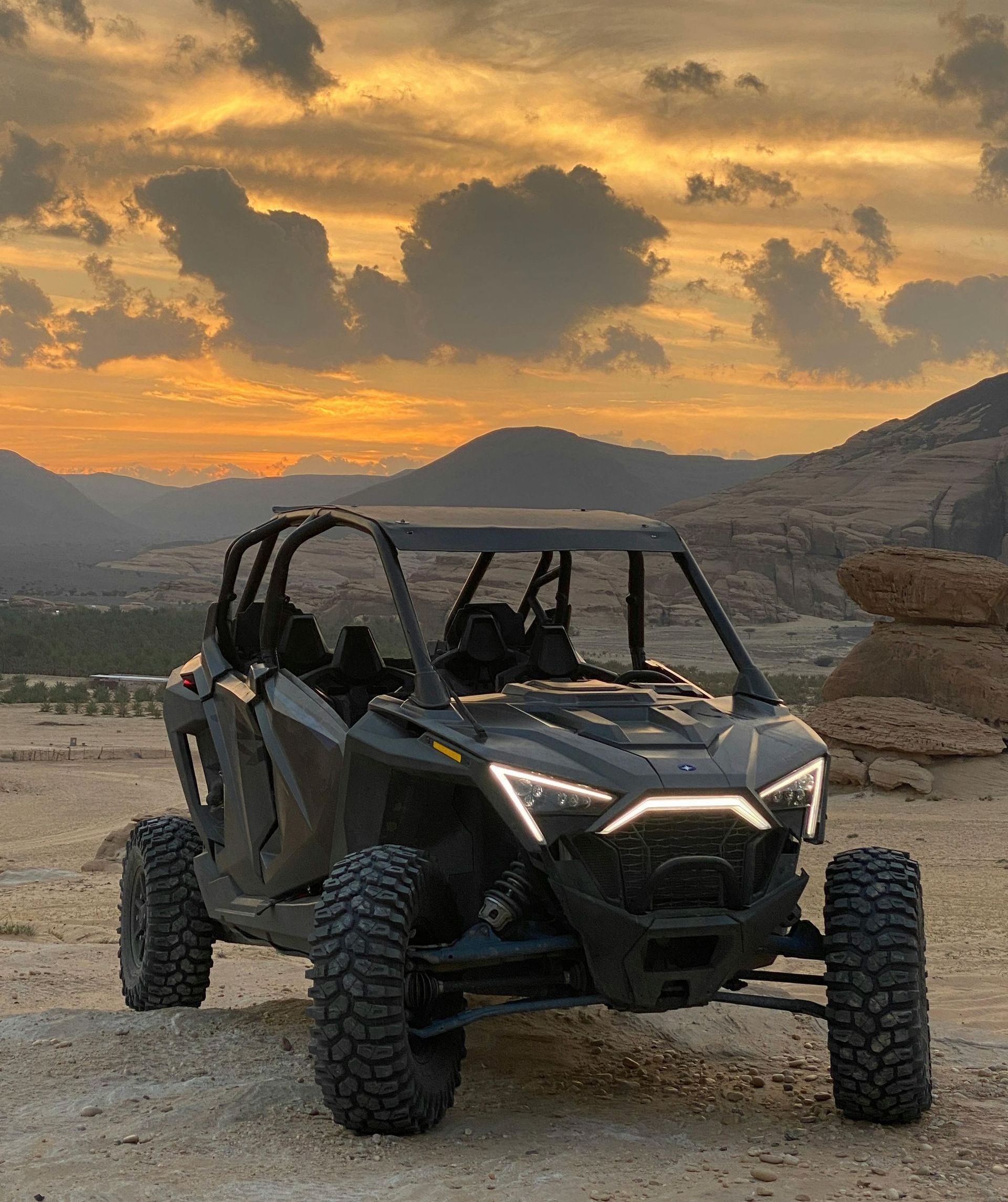 A black atv is parked in the dirt in front of mountains at sunset.