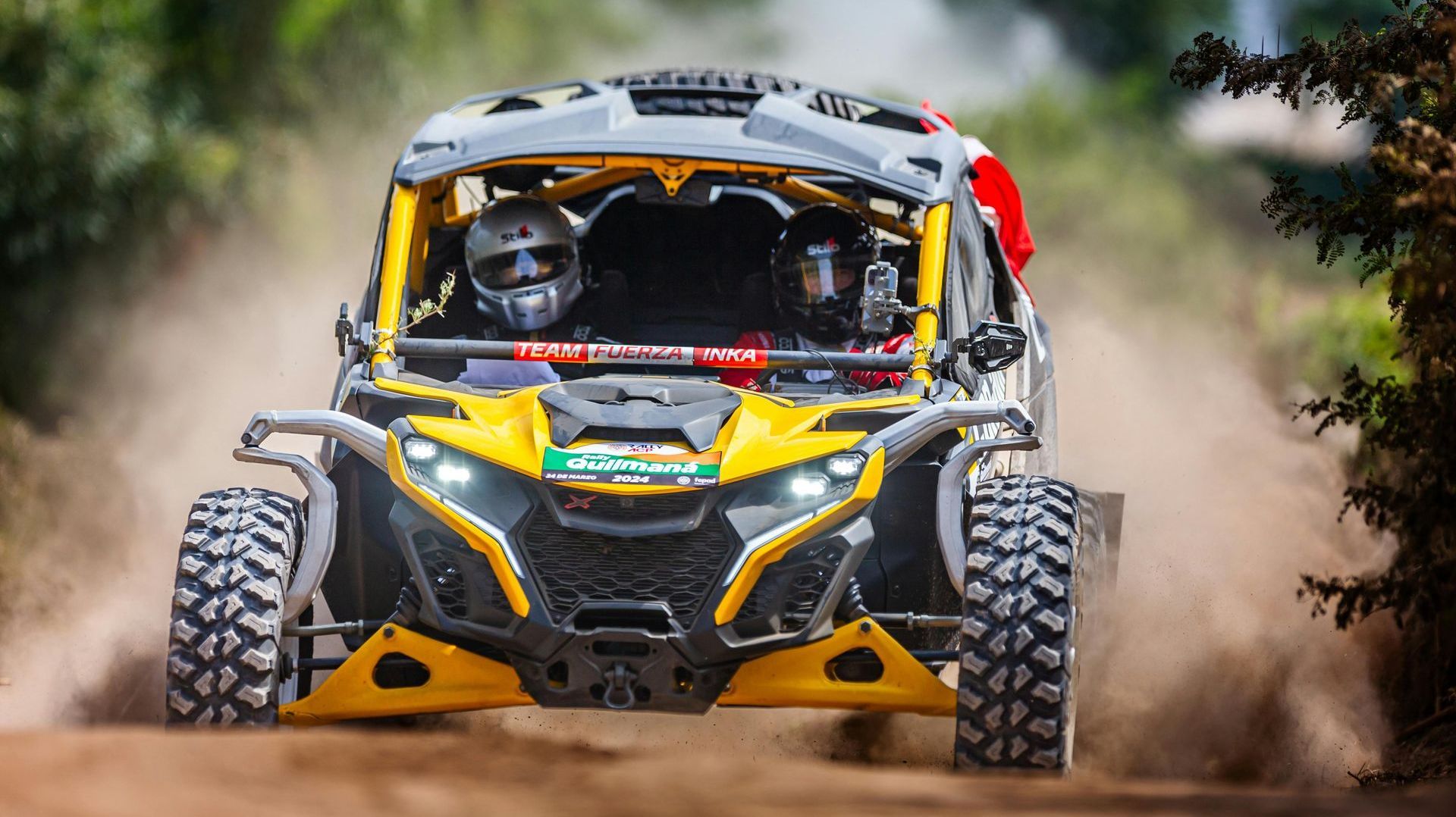 A yellow and black atv is driving down a dirt road.