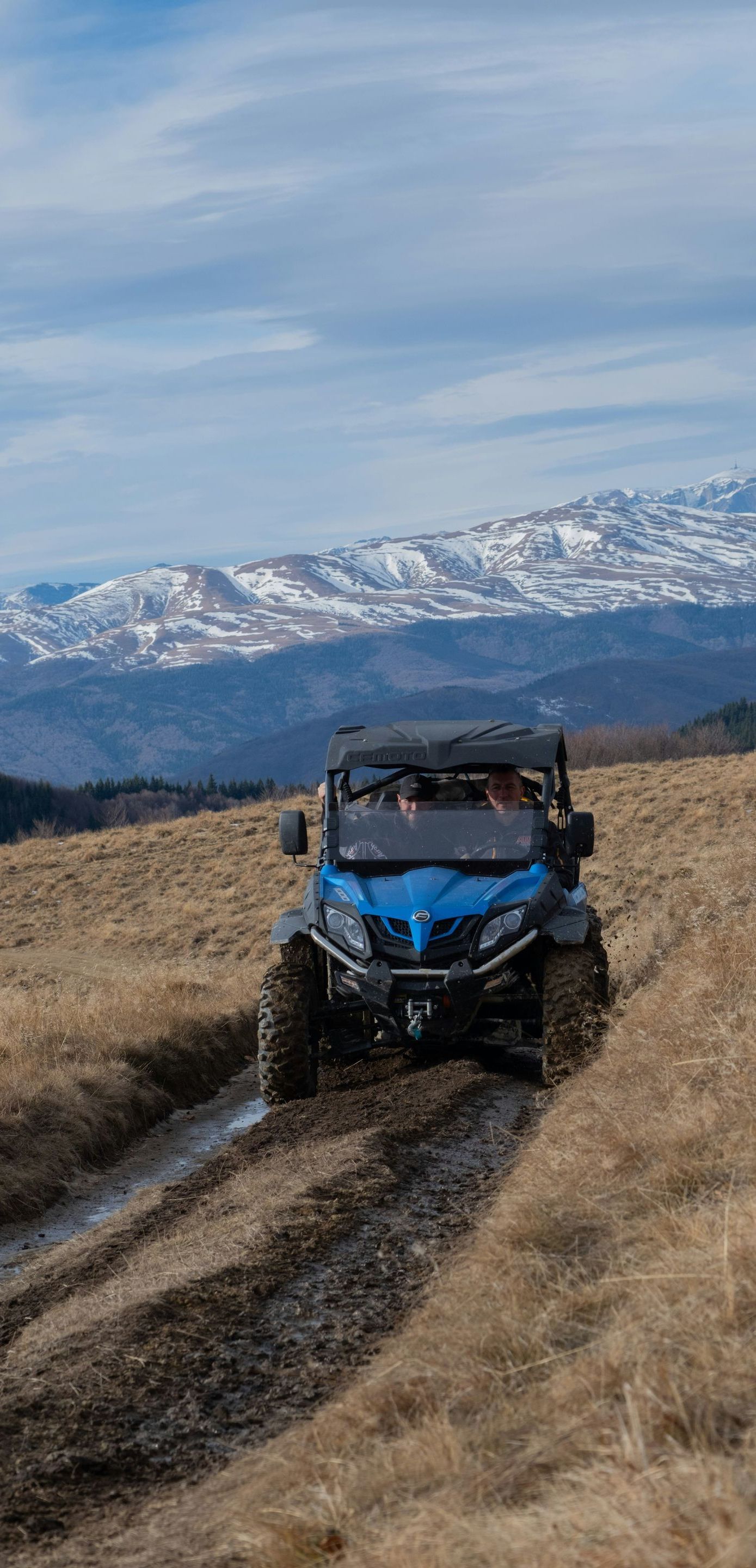A blue atv is driving down a dirt road in the mountains.