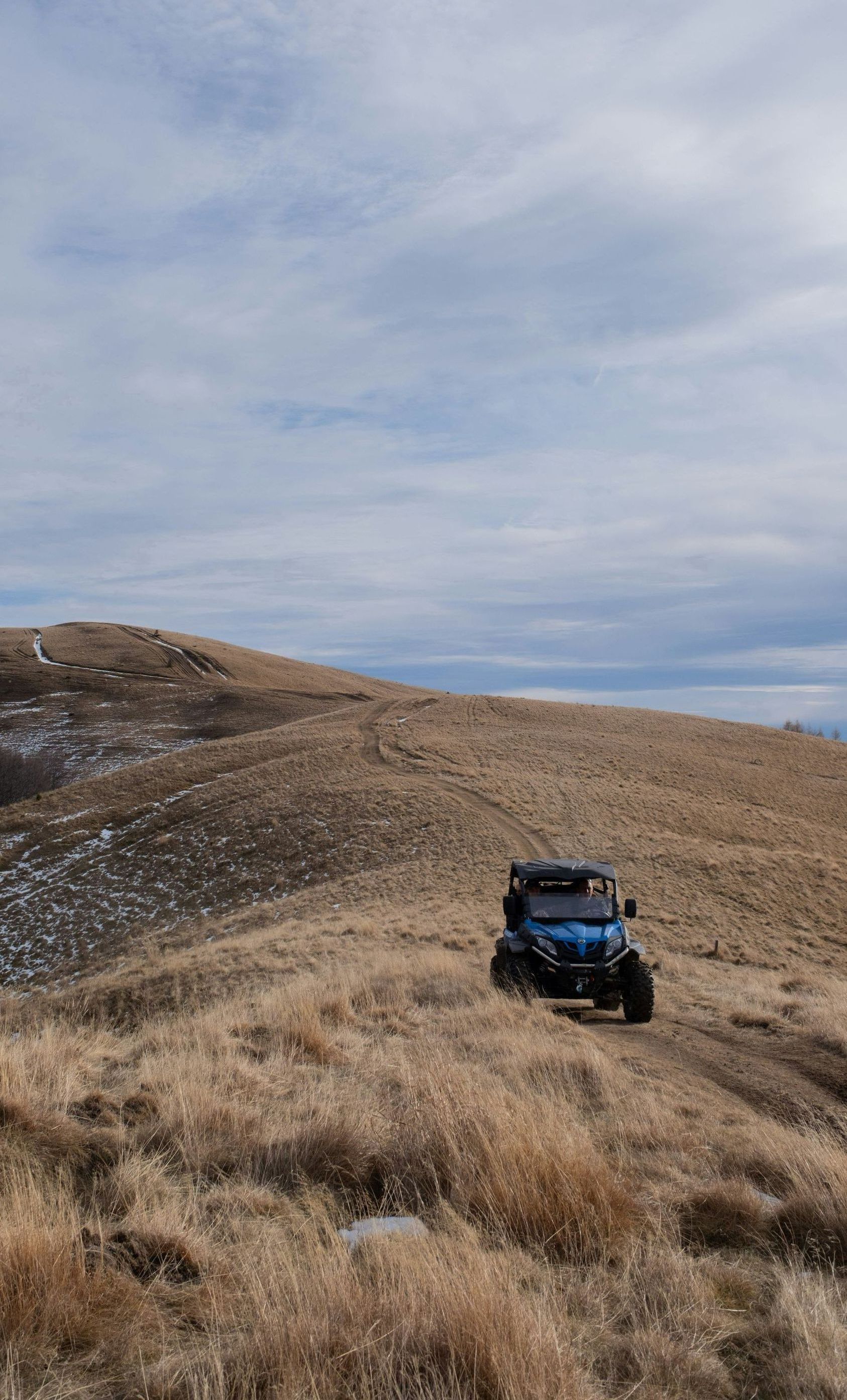 A blue utv is driving down a dirt road on top of a hill.
