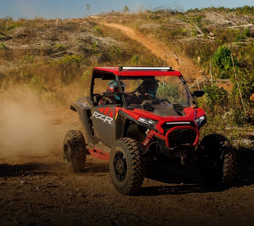 A red and black atv is driving down a dirt road.