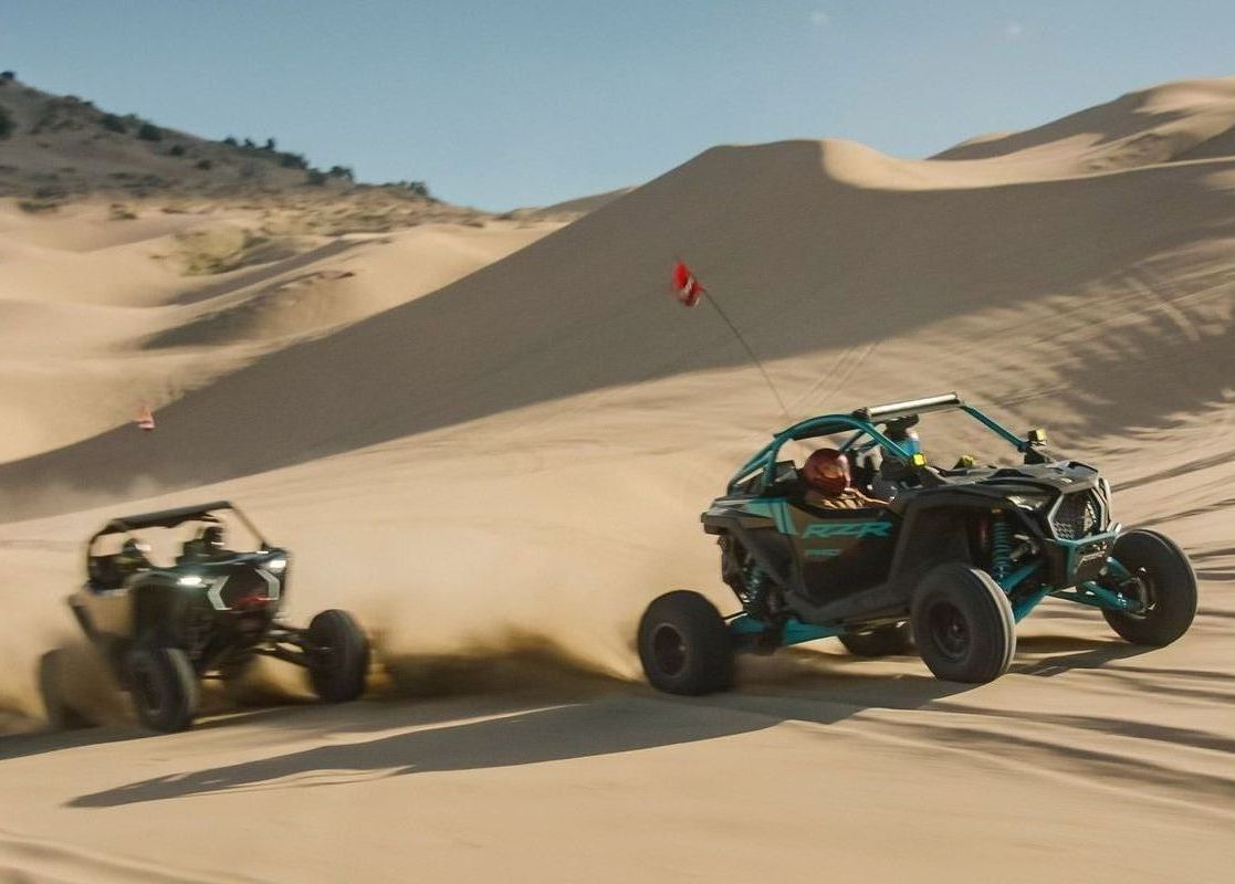 Two atvs are racing down a sand dune.