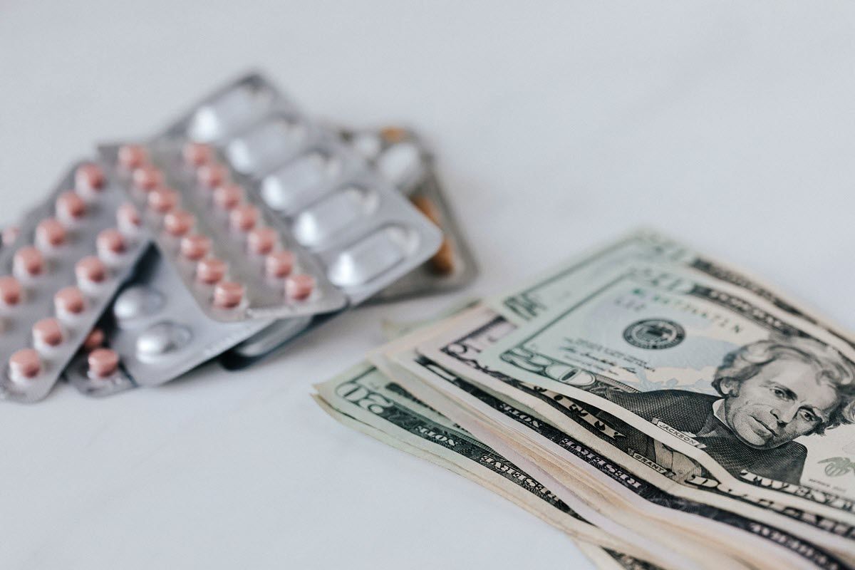 Pills in blister packs next to a stack of US dollar bills.