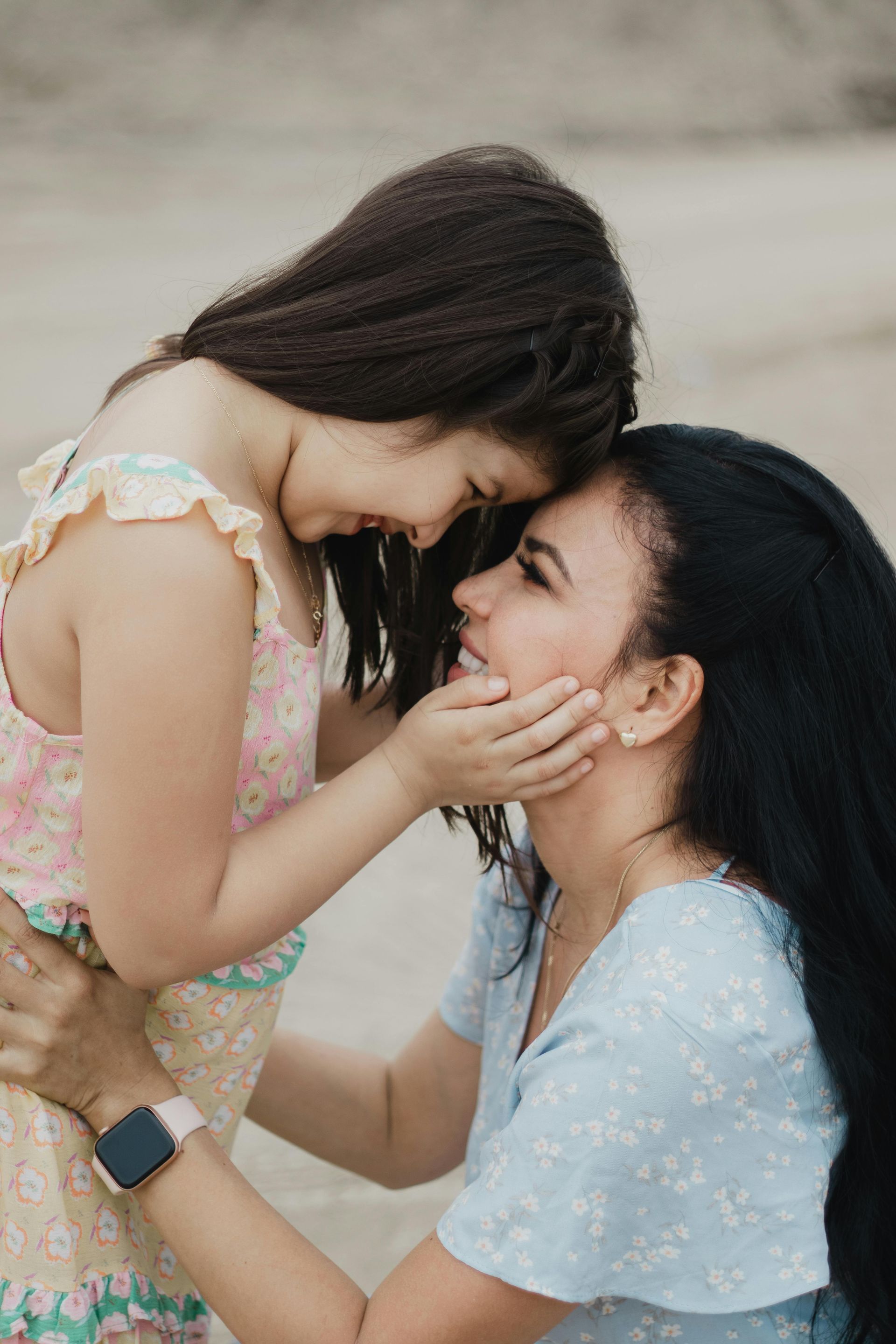 A woman and a little girl are touching their foreheads and smiling.
