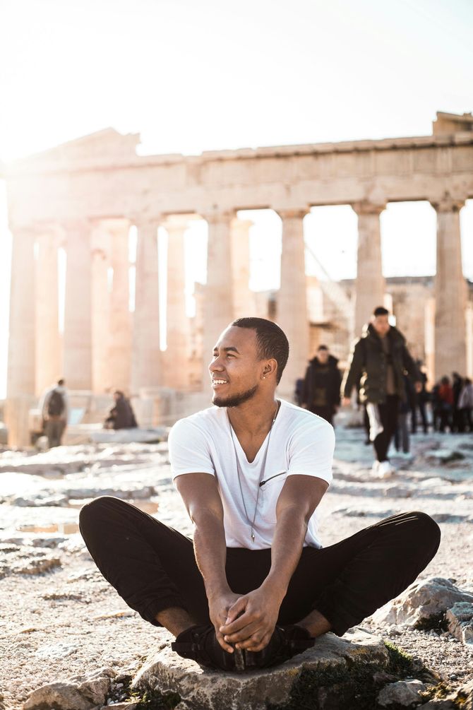A man is sitting on a rock with his legs crossed in front of a building.