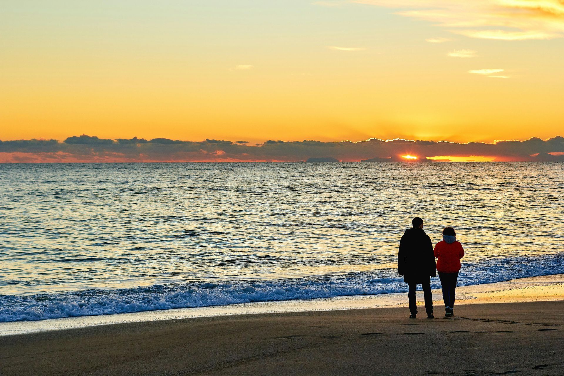 A man and a woman are walking on the beach at sunset
