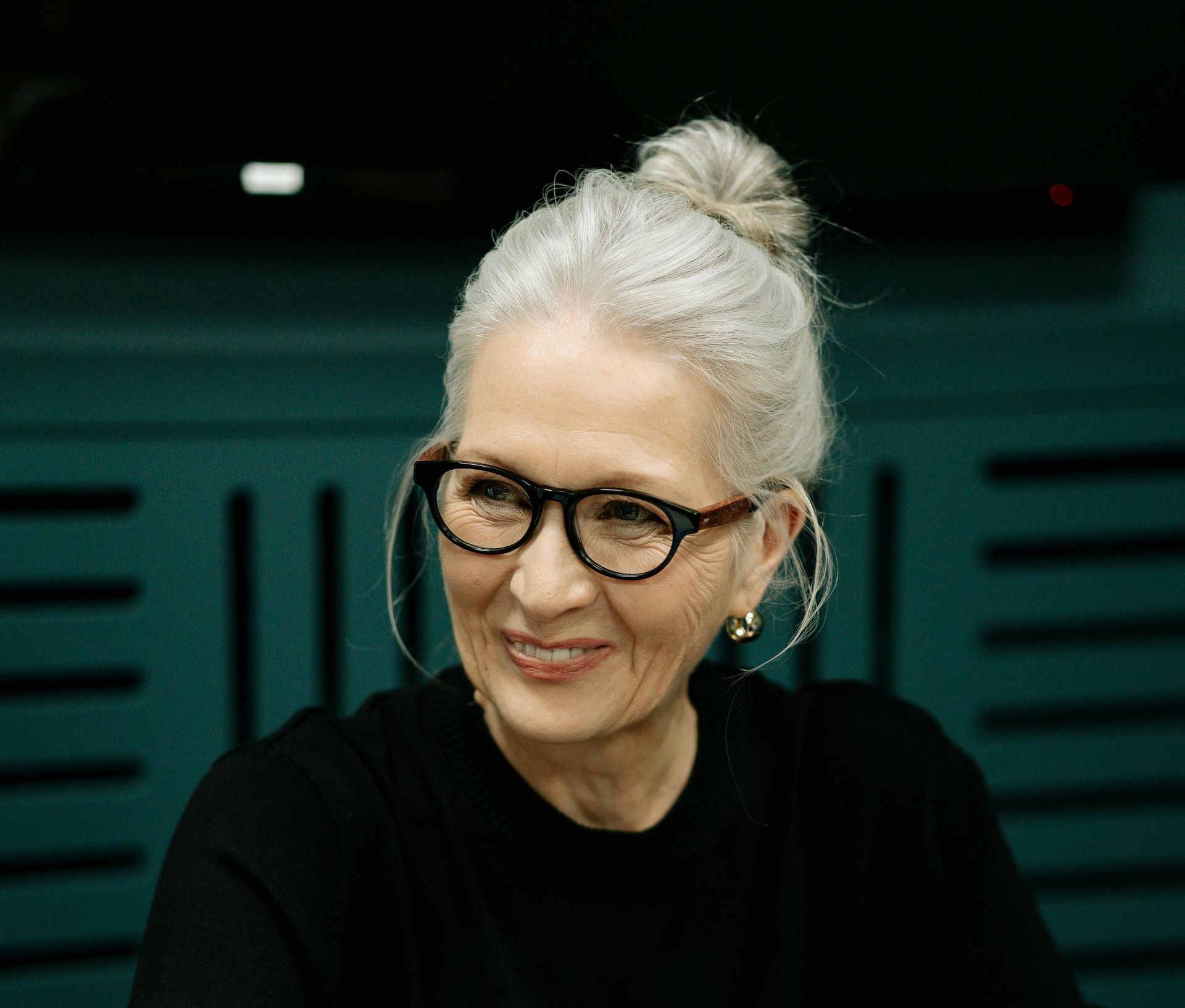 An older woman wearing glasses and a bun is smiling.