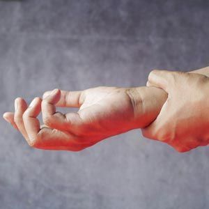 A hand gripping the wrist of another hand against a gray background.