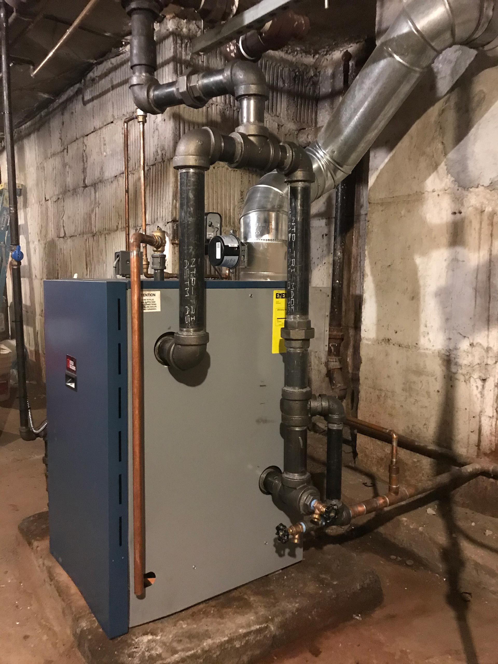 A blue boiler is sitting in a basement surrounded by pipes.