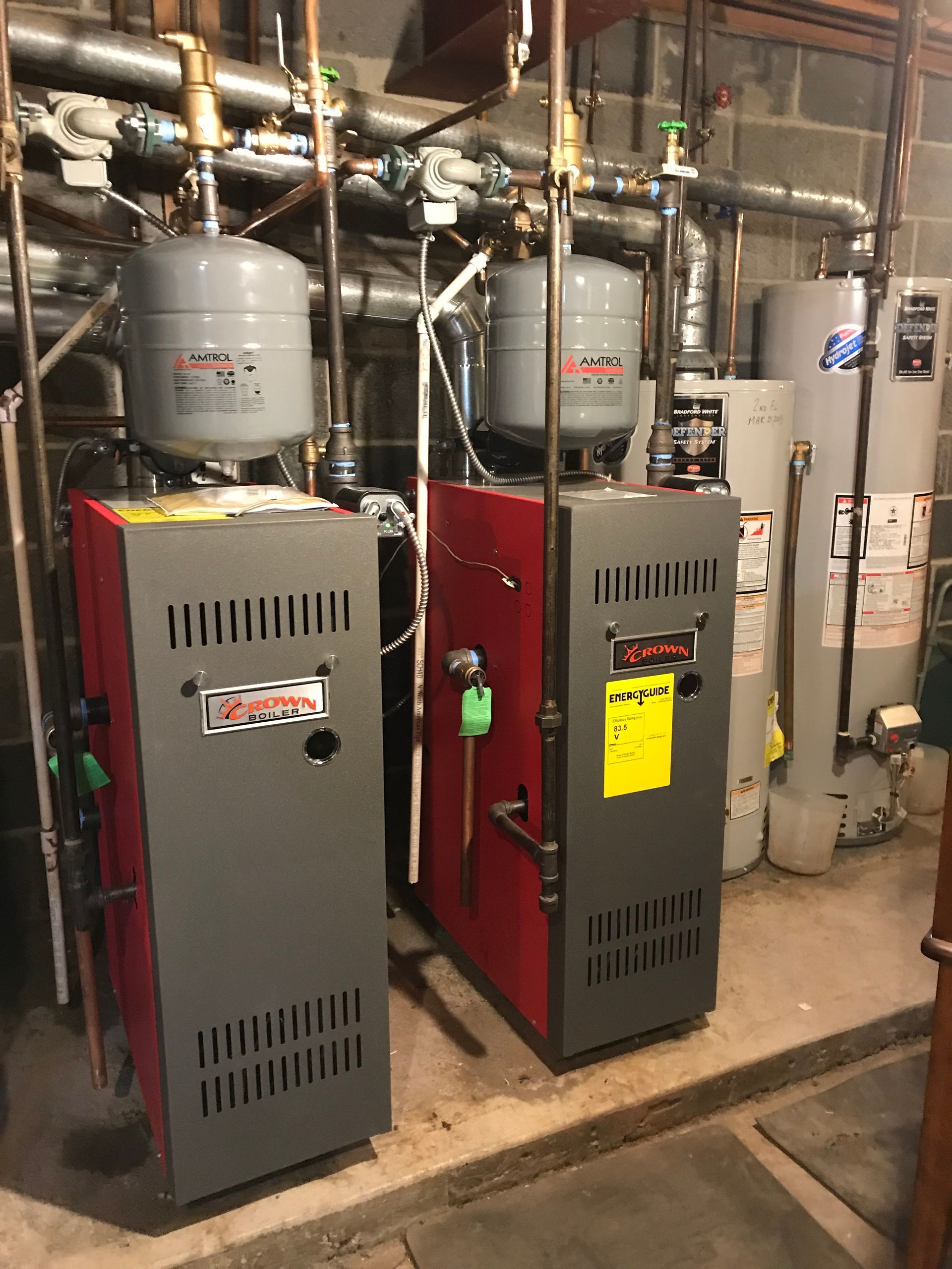 Two boilers are sitting next to each other in a basement.