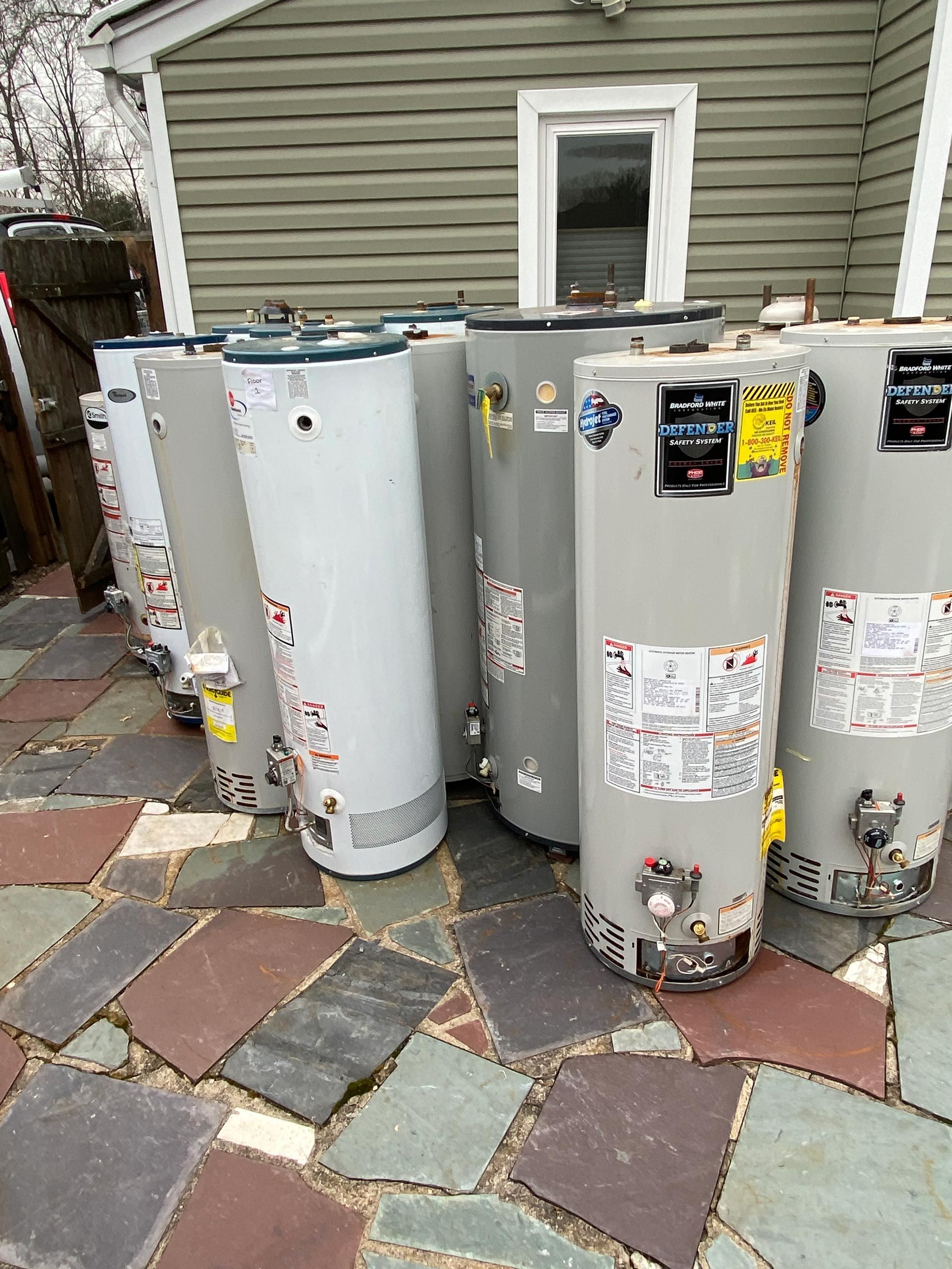 A row of water heaters are sitting on a tiled patio in front of a house.