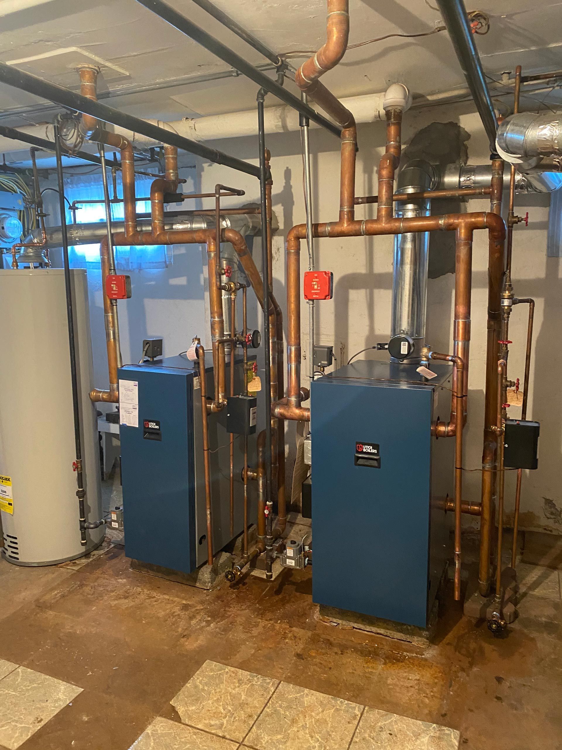 Two blue boilers are sitting next to each other in a room with pipes.