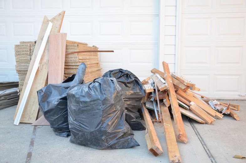 A pile of wood and trash bags on the sidewalk in front of a garage door.
