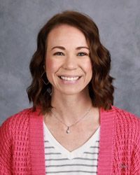 A woman wearing a pink sweater and a striped shirt is smiling for the camera.