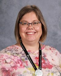 A woman wearing glasses and a lanyard is smiling for the camera.