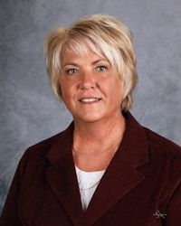 A woman in a maroon jacket and white shirt is smiling for the camera.