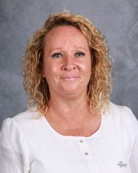 A woman with curly hair is wearing a white shirt and smiling for the camera.