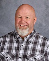 A bald man with a beard is wearing a plaid shirt and smiling for the camera.