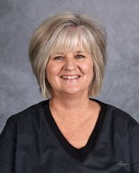 A woman in a black scrub top is smiling for the camera.