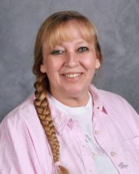 A woman with a braid is wearing a pink shirt and smiling for the camera.