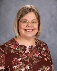 A woman wearing glasses and a purple sweater is smiling for the camera.