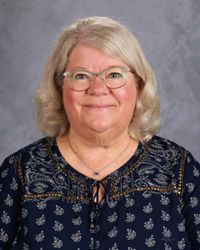 A woman wearing glasses and a jacket is smiling for the camera.