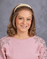 A woman in a black  jacket and blueshirt is smiling for the camera.