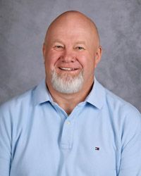 A bald man with a beard is wearing a plaid shirt and smiling for the camera.