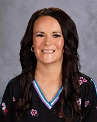 A woman in a black& white scrub top is smiling for a picture.