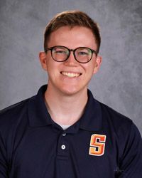 A young man with glasses wearing a black shirt is smiling for the camera.