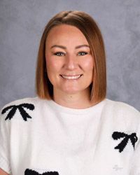 A woman with long brown hair in a pink shirt is smiling for the camera.