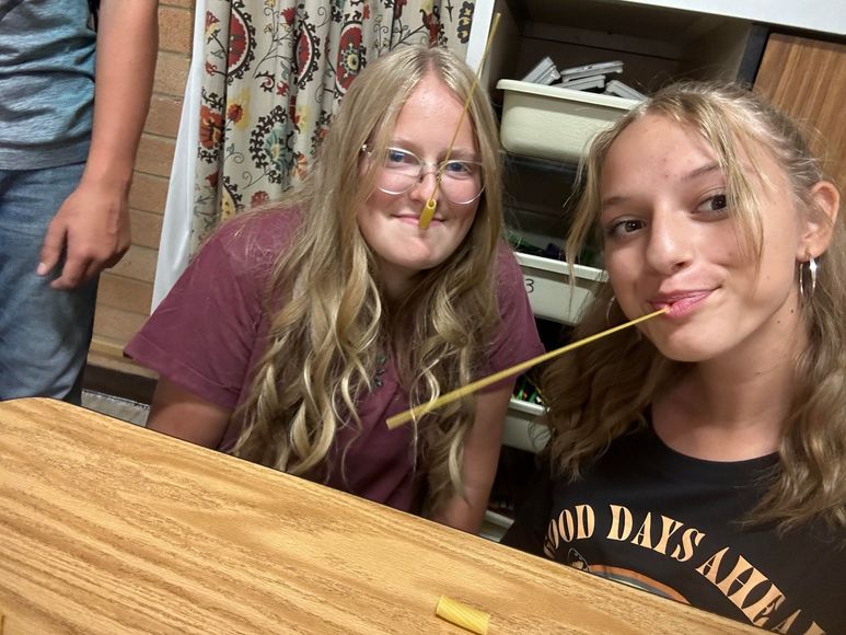 two girls are sitting at a table with a yellow string in their mouths .