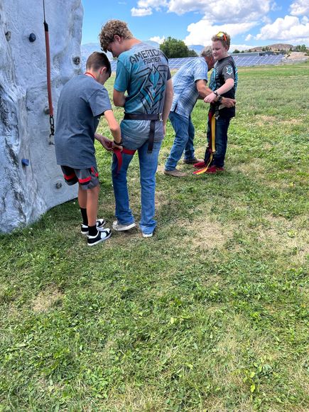 a group of people are standing in a grassy field in front of a climbing wall .