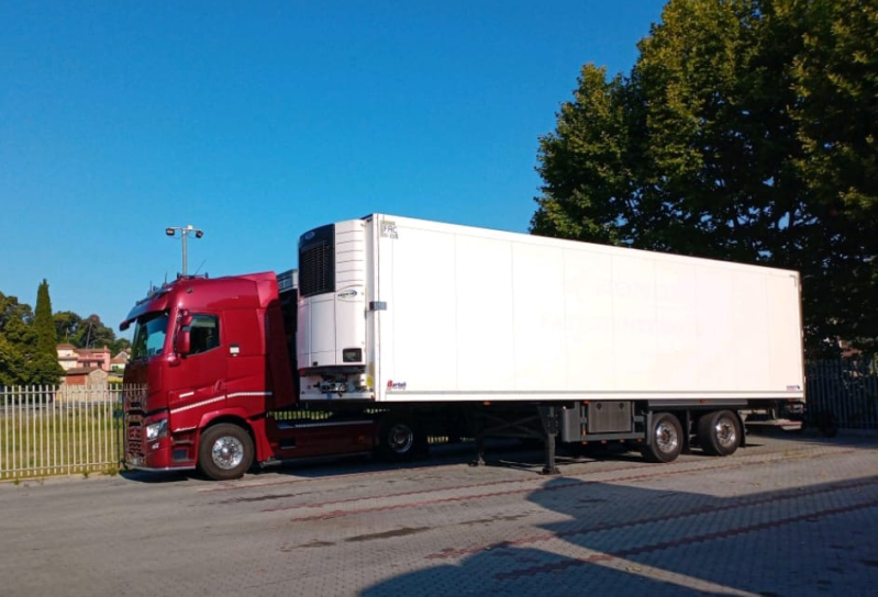 Un camion rosso e bianco parcheggiato all'aperto sul marciapiede sotto un cielo azzurro e terso.