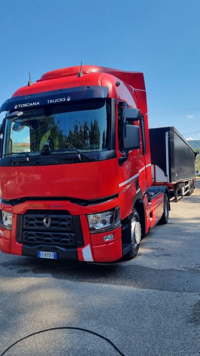 Camion rosso con rimorchio sul marciapiede sotto un cielo azzurro.