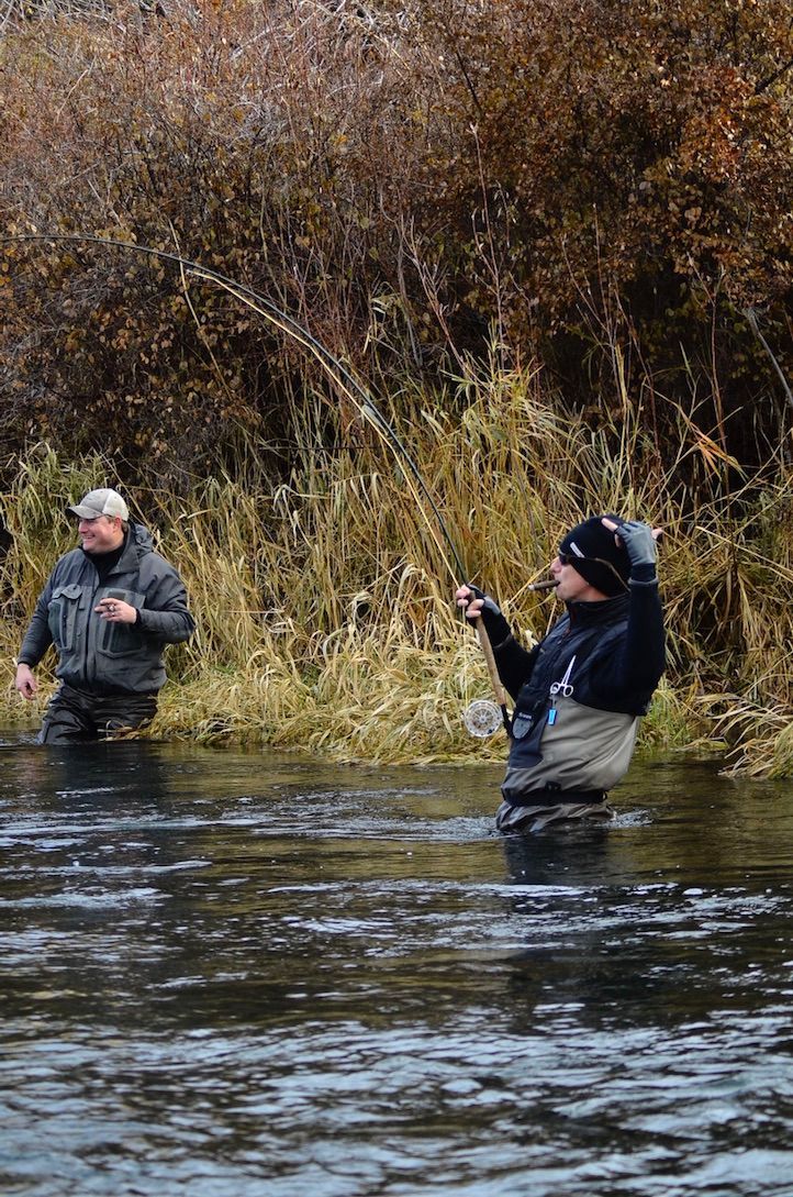 Two men are fishing in a river with fishing rods.