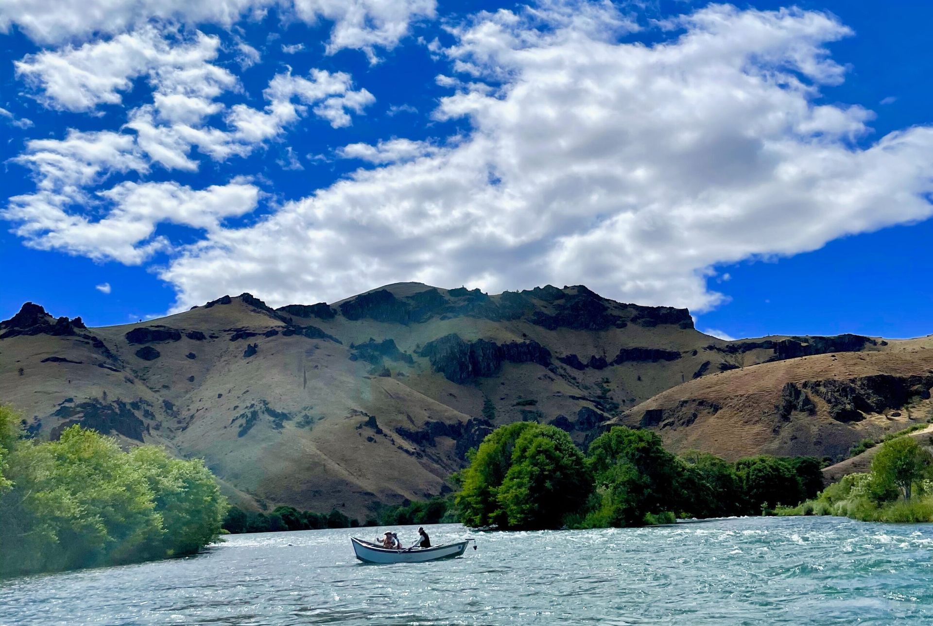 Two people in a boat on a river with mountains in the background